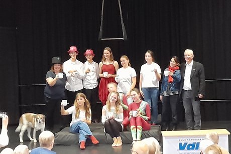 Zum Abschluss treten die jugendlichen Artisten auf die Bühne und bedanken sich beim Publikum der Mitglieder des VdK. Alle Teilnehmer halten dabei einen Trinkbecher des VdK in die Höhe