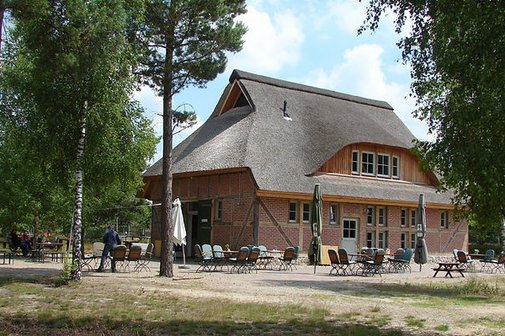 Heidehaus Nemitz Das Heide-Haus in der Nemitzer Heide: Ein reetgedecktes Backsteingebäude im ländlichen Stil mit Außenbestuhlung im Vordergrund, umgeben von Bäumen.