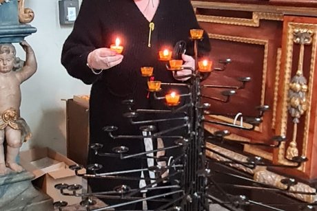 Eine Person zündet eine Kerze auf einem Kerzenständer in der Klosterkirche an