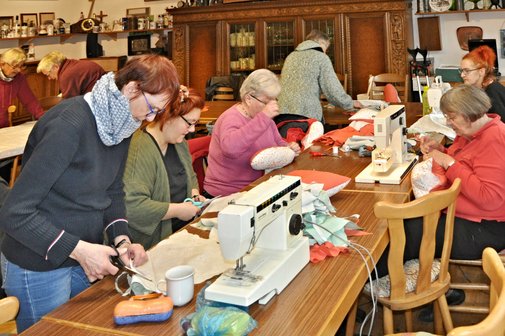 Mitglieder des Kreisverbandes Celle sitzen und stehen an Tischen. Auf den Tischen sind Nähmaschinen und weitere Utensilien zu sehen, mit denen die Herzkissen hergestellt werden. Im Vordergrund des Fotos sind Anja Bartelt, Bernadette Wolski und Rosemarie Clasen aus dem Ortsverband Celle-Altstadt zu sehen.