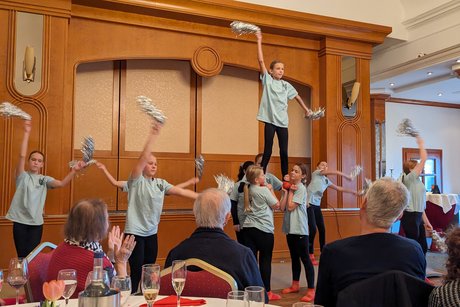 Die Cheerleading-Gruppe zeigt eine Figur mit einer Teilnehmerin auf den Händen von drei anderen.