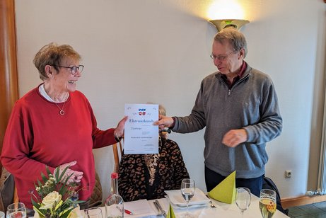 Der Vorsitzende Dieter Buhmann &uuml;berreicht die Ehrenurkunde f&uuml;r 25-j&auml;hrige Mitgliedschaft im VdK an unser Mitglied Rosemarie Landenberger. Zu sehen sind die beiden Personen im Gastraum von Seekamps Centralhallen.