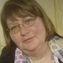 Portr&auml;t einer Frau mit braunen Haaren, Pony und Brille, die ein gemustertes Tuch tr&auml;gt."
