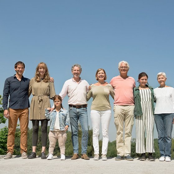 Menschen verschiedenen Alters mit und ohne Behinderung blicken lächelnd in die Kamera Menschen verschiedenen Alters mit und ohne Behinderung stehen untergehakt und lächelnd in einer Reihe in der Sonne