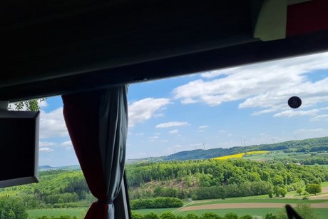 Blick aus einem Busfenster auf eine grüne, hügelige Landschaft