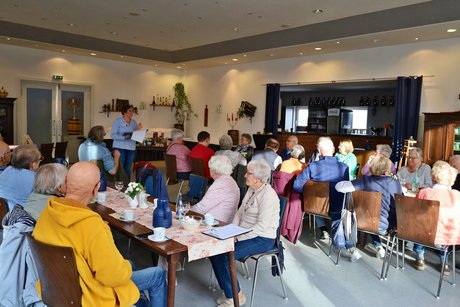 Die Teilnehmerinnen und Teilnehmer unseres monatlichen Treffens sitzen an Tischen und h&ouml;ren dem ergreifenden und r&uuml;hrenden Vortrag von Frau Julia Dittel zu.