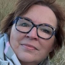 Eine dunkelhaarige Frau mit Brille und einem grau wei&szlig;en Schal