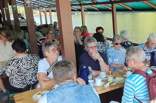 Mitglieder sitzen an Tischen auf dem Floss bei Kaffee und Kuchen