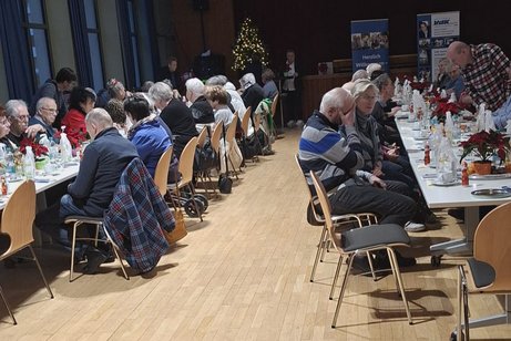 Weihnachtlich geschm&uuml;ckter Festsaal mit Menschen an langen Tischreihen