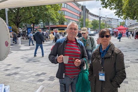 Gespräche und Kaffee am VdK-Stand Das Bild zeigt einen Mann und eine Frau, die auf einer belebten Fußgängerzone in Hannover stehen. Der Mann auf der linken Seite hält einen Kaffeebecher in der Hand.