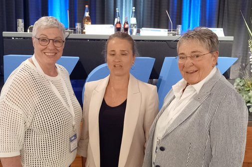 Birgit Becker, Verena Bentele und Jutta Da Corte stehen in einer Festhalle zusammen