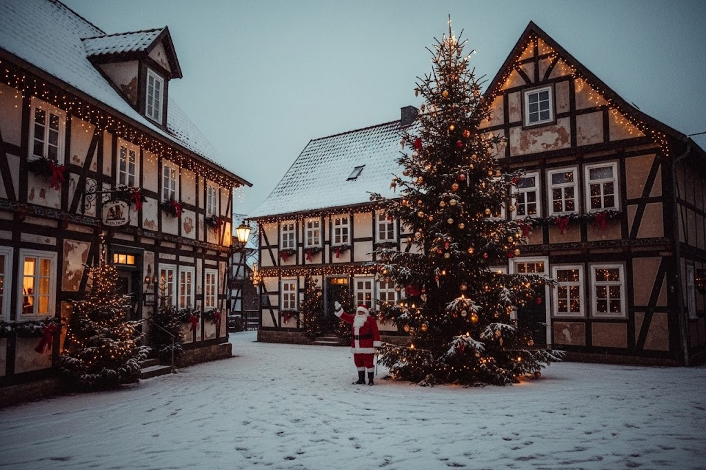 Niedersächsische Fachwerkhäuser, vor denen ein großer Weihnachtsbaum steht. Neben dem Baum steht der Weihnachtsmann und winkt. Es liegt Schnee.