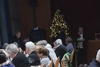 Weihnachtlich geschm&uuml;ckter Festsaal mit Menschen an langen Tischreihen