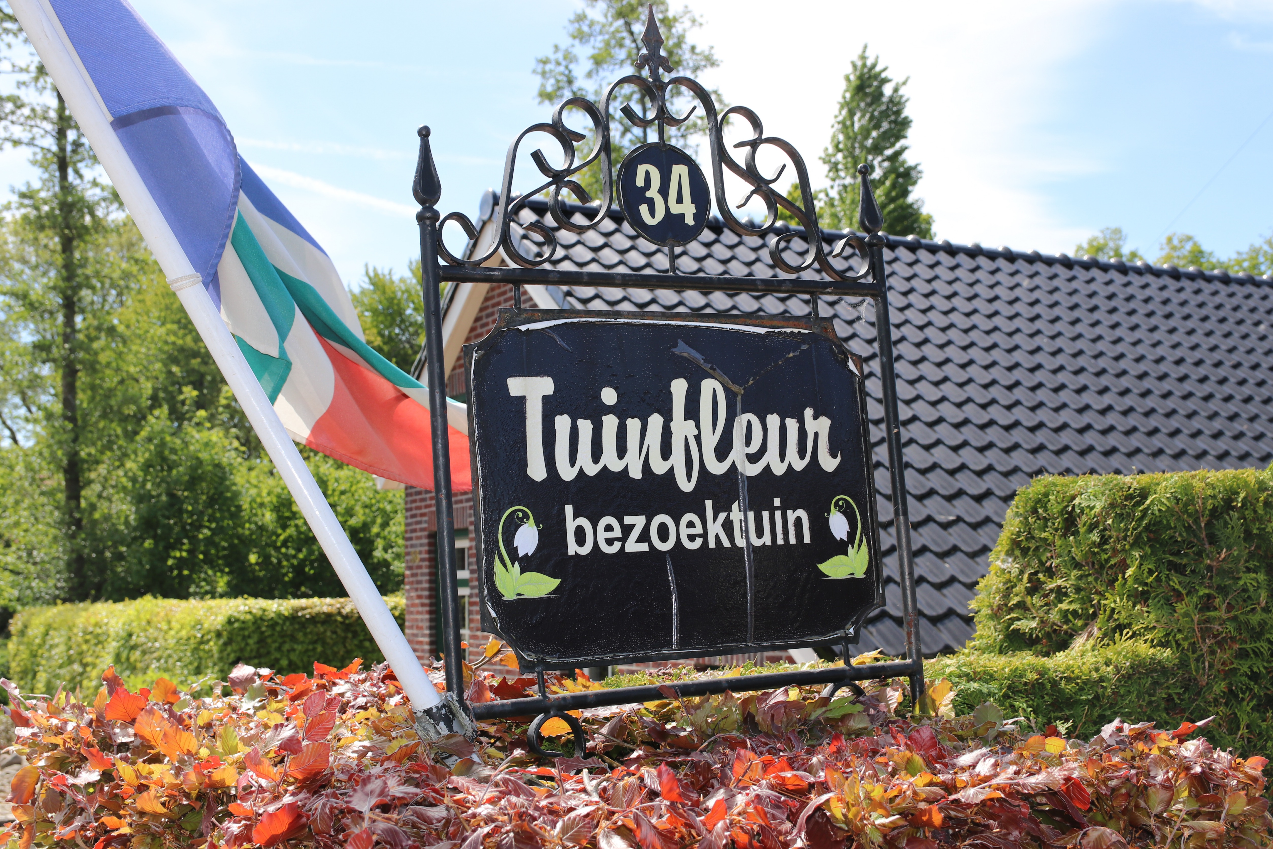 Schaugarten Tuinfleur Schild mit der Bezeichnung Tuinfleur bezoektuin vor einem Hausdach.