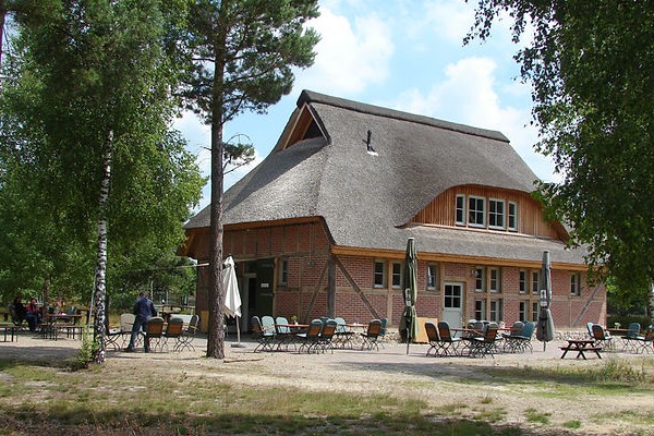 Das Heide-Haus in der Nemitzer Heide: Ein reetgedecktes Backsteingeb&auml;ude im l&auml;ndlichen Stil mit Au&szlig;enbestuhlung im Vordergrund, umgeben von B&auml;umen.