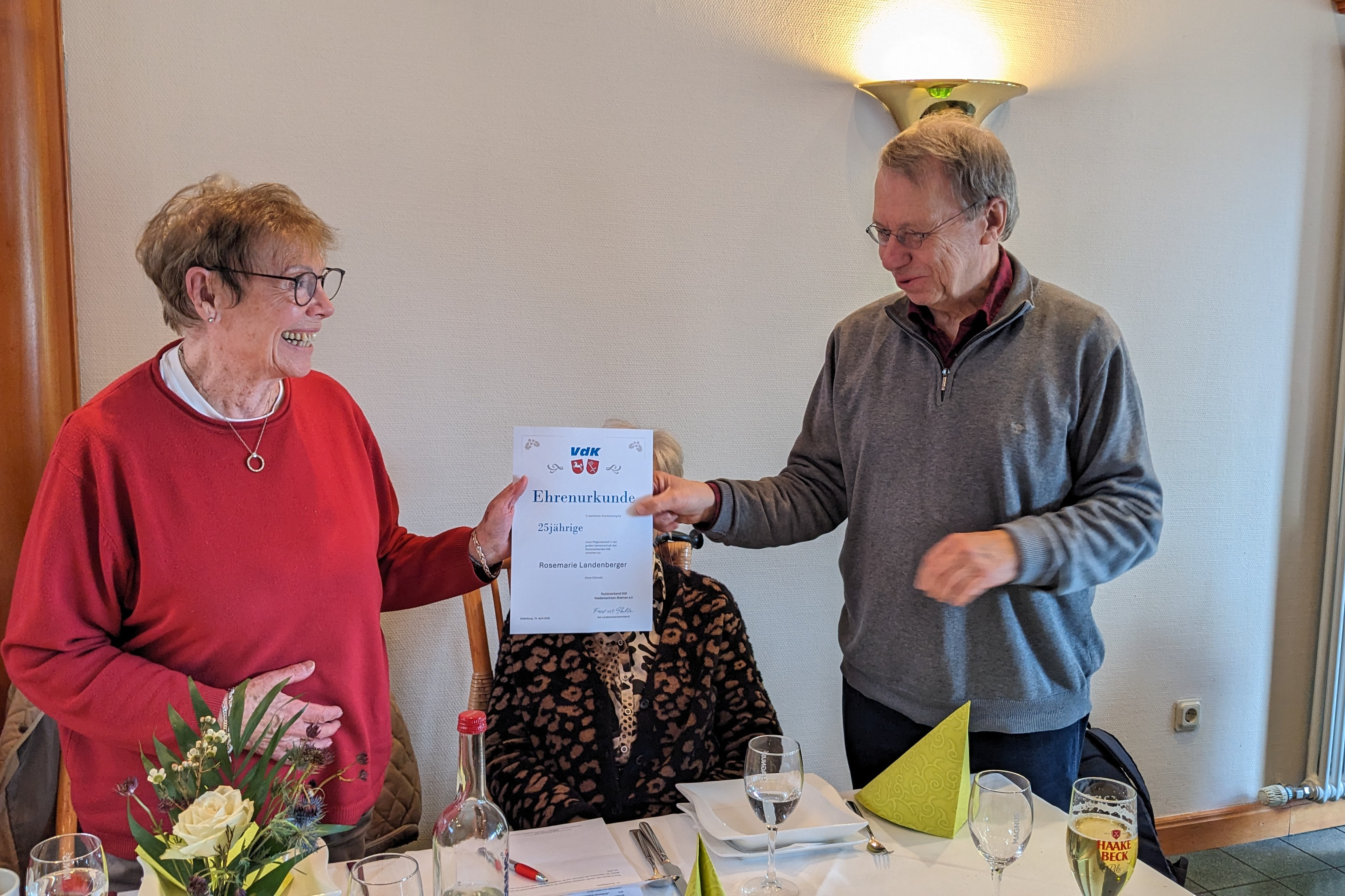 Der Vorsitzende Dieter Buhmann &uuml;berreicht die Ehrenurkunde f&uuml;r 25-j&auml;hrige Mitgliedschaft im VdK an unser Mitglied Rosemarie Landenberger. Zu sehen sind die beiden Personen im Gastraum von Seekamps Centralhallen.